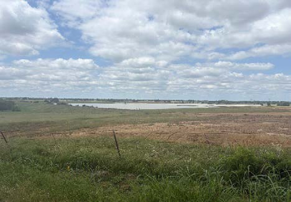 Open pasture at Taylor Ranch in Gunter TX with the onsite reservoir visible on the horizon under a cloudy sky