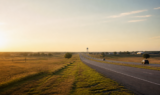 A North Texas divided highway at golden hour, open prairie on one side and a distant water tower on the other.
