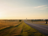 A North Texas divided highway at golden hour, open prairie on one side and a distant water tower on the other.