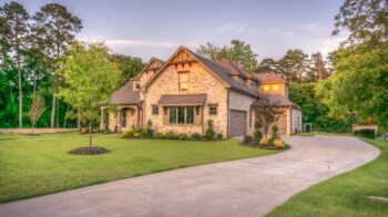 Modest country home on a wooded Grayson County-style lot at warm late-afternoon light, green lawn and driveway under a soft sunset sky—no people, no text