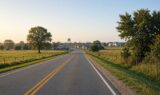 Two-lane North Texas highway approaching a small town with a water tower at golden hour, representing Gunter, Texas