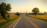 Golden-hour view of a North Texas two-lane highway approaching a small city with a water tower on the horizon, suggesting Van Alstyne along the U.S. 75 corridor