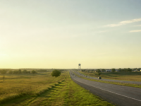 North Texas highway at golden hour through prairie near a water tower, documentary view of the Denison–Sherman growth corridor