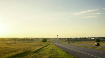 North Texas highway at golden hour through prairie near a water tower, documentary view of the Denison–Sherman growth corridor
