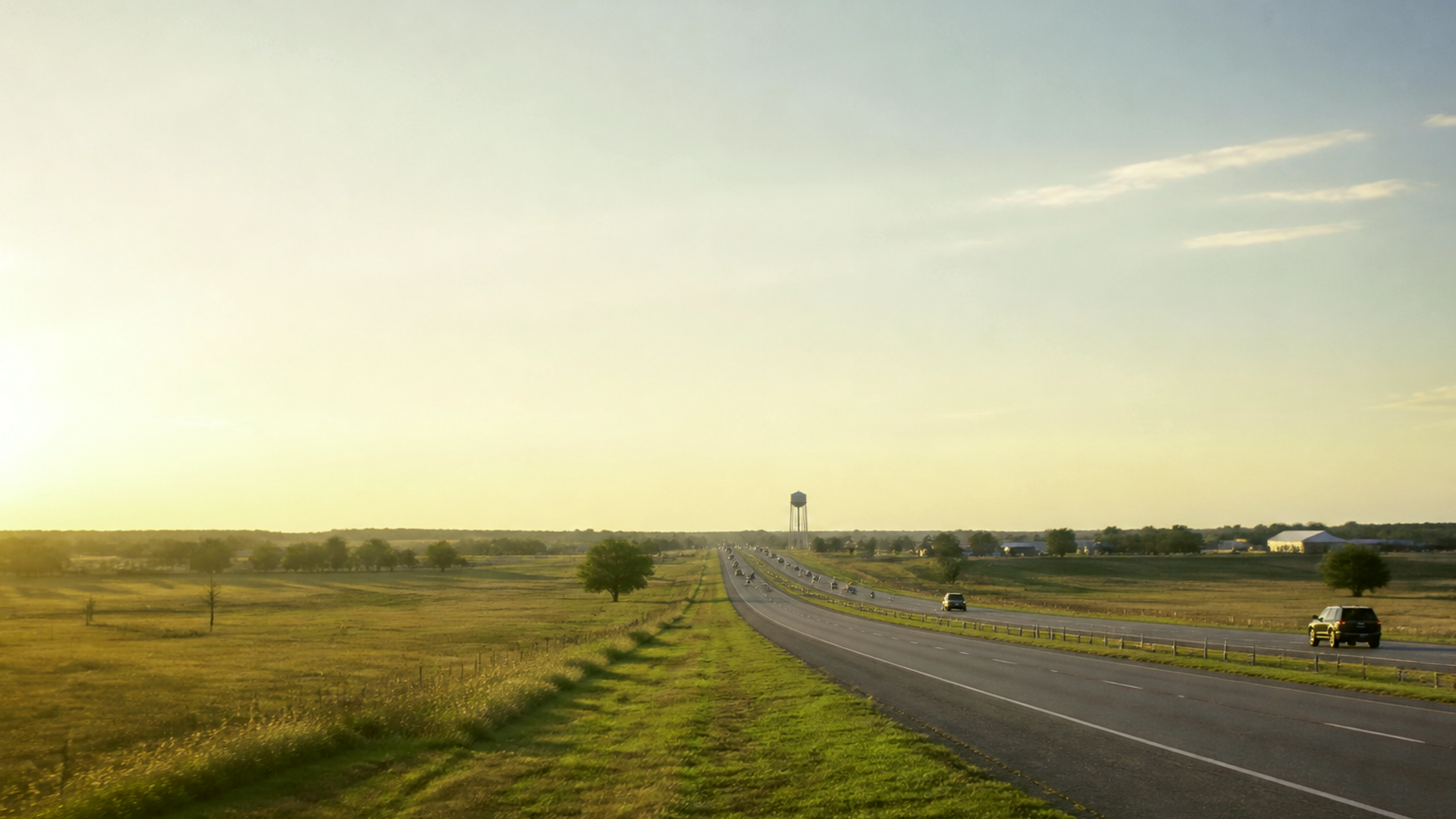 North Texas highway at golden hour through prairie near a water tower, documentary view of the Denison–Sherman growth corridor