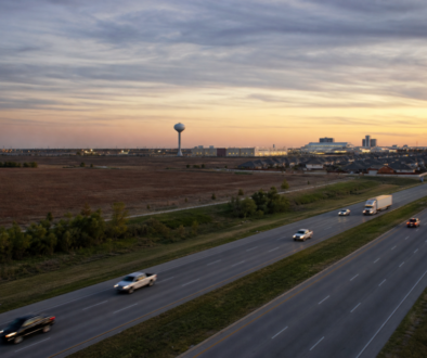 U.S. 75 corridor at dusk near Sherman, with prairie, a water tower, and industrial lights on the horizon.