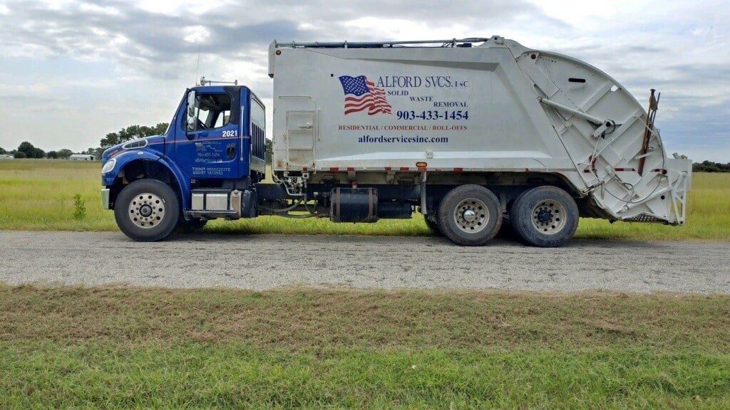Blue and white Alford Services residential trash truck parked on a gravel road