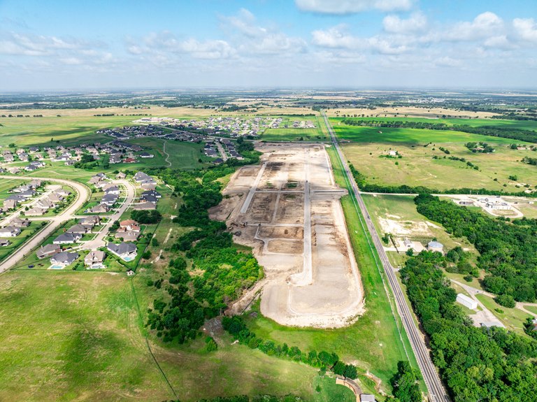 Aerial view of The Bridges at Preston Crossings in Gunter TX showing finished homes on the left and a newly graded section of streets and lots beside the highway