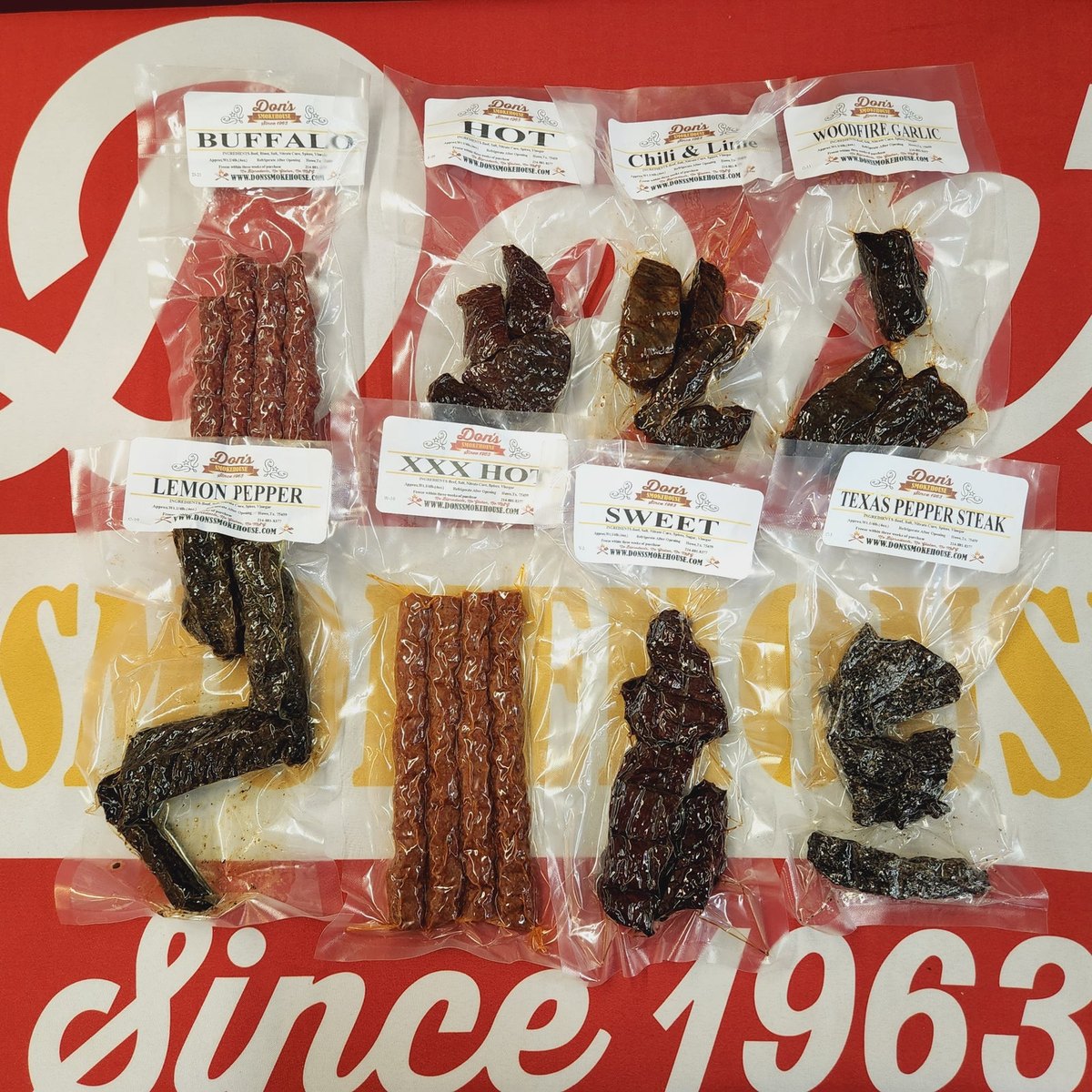 Bags of Don's Smokehouse jerky and snack sticks laid out on a red Since 1963 backdrop