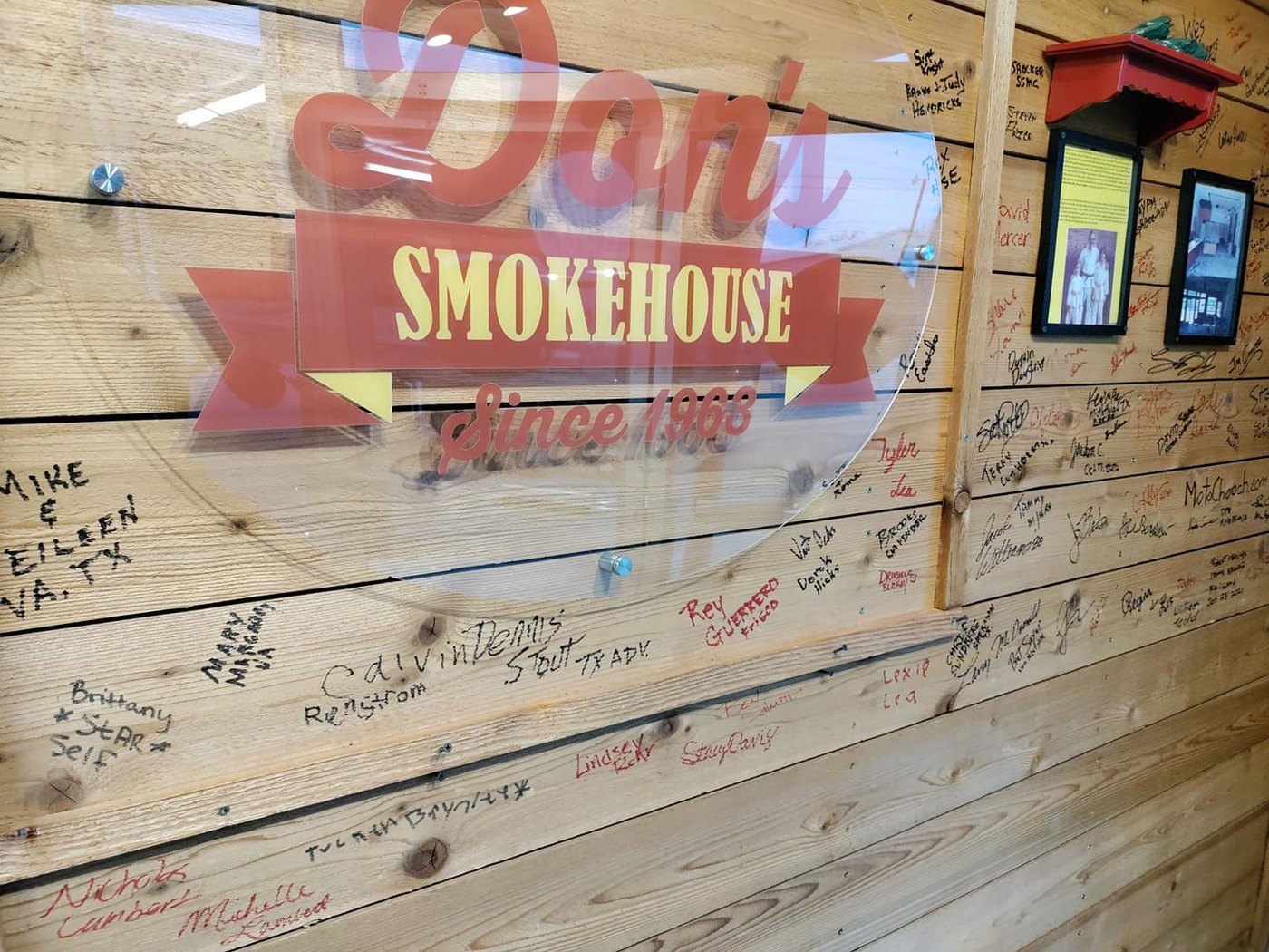 Don's Smokehouse sign on a wood-plank wall covered in customer signatures in Howe, TX