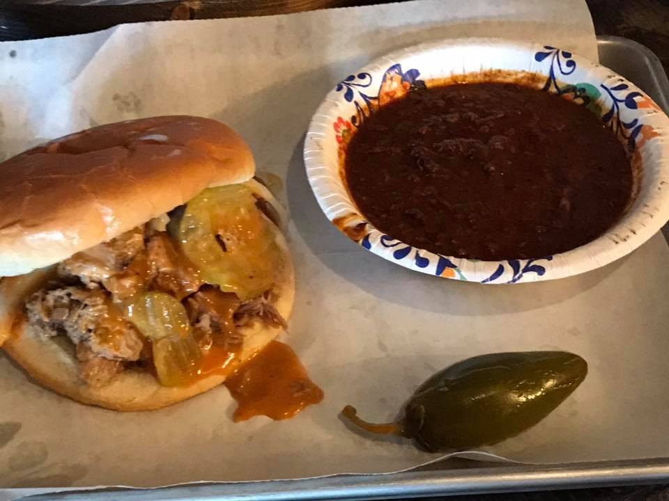 Barbecue sandwich with pickles, a jalapeño, and a side bowl on a tray at Hickory House Bar-B-Que Denison