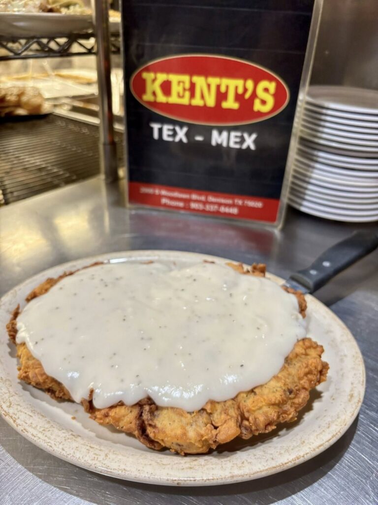 Chicken fried steak smothered in white cream gravy on a plate in front of a Kent's Tex-Mex sign card in Denison