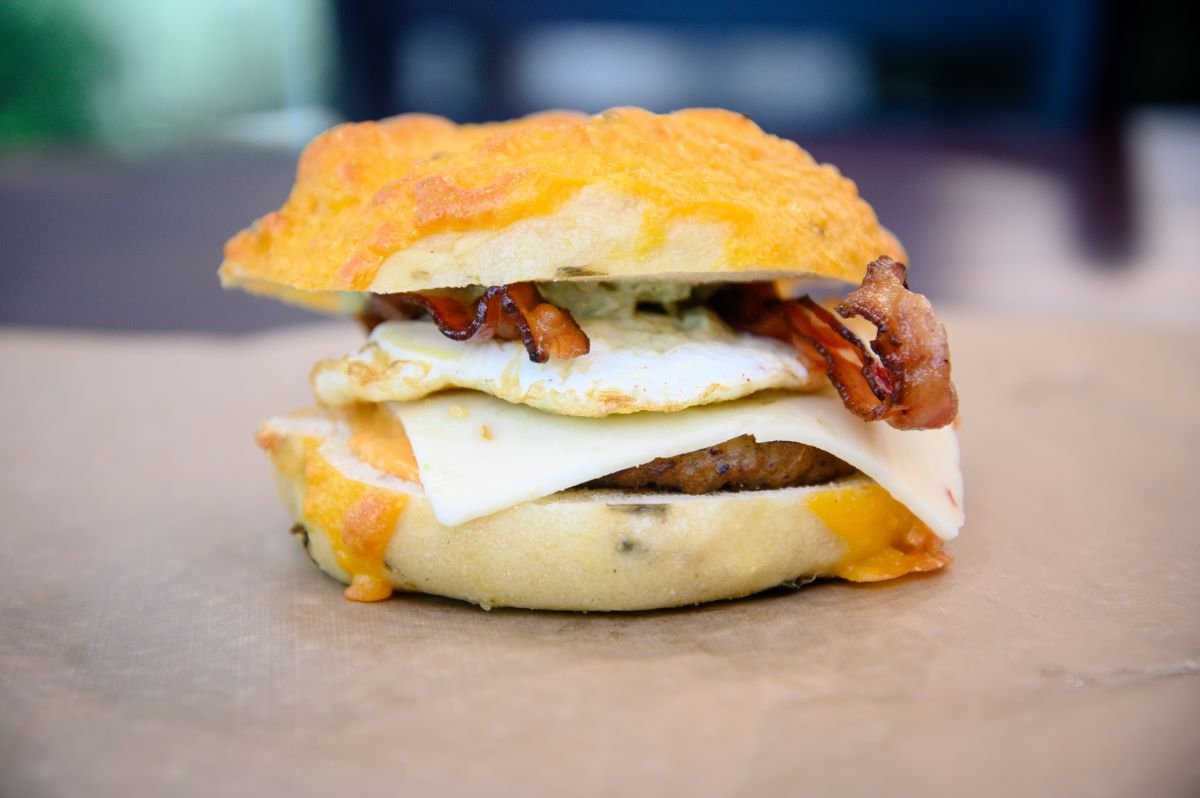 Breakfast bagel sandwich stacked with egg, bacon and melted cheese on a cheese-topped bagel at Legacy Bagels