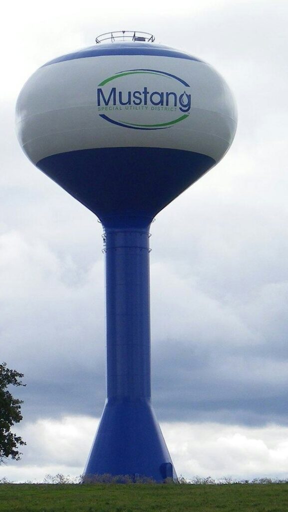 Blue and white Mustang Special Utility District water tower against a cloudy sky