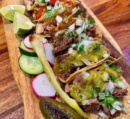 Beef tacos with green salsa, onion, and cilantro next to radish, cucumber, and a grilled jalapeño at Street Tacos in Howe