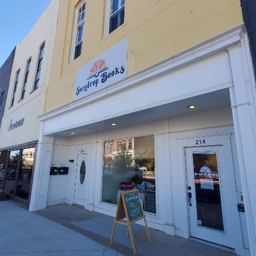 Sundrop Books storefront at 214 W. Main St. in downtown Denison, with its sunburst sign above the door and a chalkboard sign on the sidewalk
