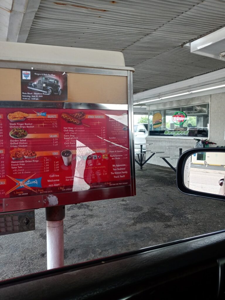 Stall menu board with baskets, sides, chili dogs, and shakes at Watson's Drive In Denison